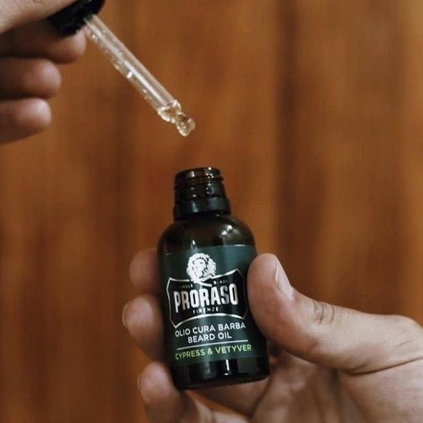 En hand som håller en flaska Proraso Cypress & Vetyver skäggolja för att mjukgöra skägget.