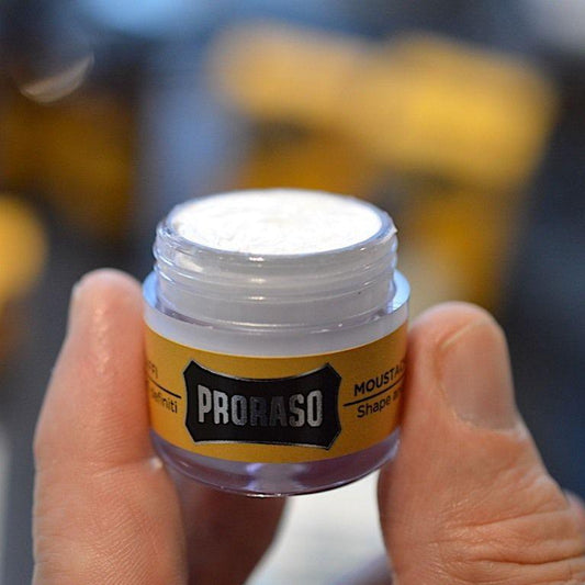 En person applicerar Proraso mustaschvax från en liten burk med en mustaschkam.