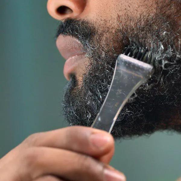 En man putsar sitt skägg med en Just for Men skäggtrimmer och applicerar Skäggfärg - Mediumbrun naturlig färg.